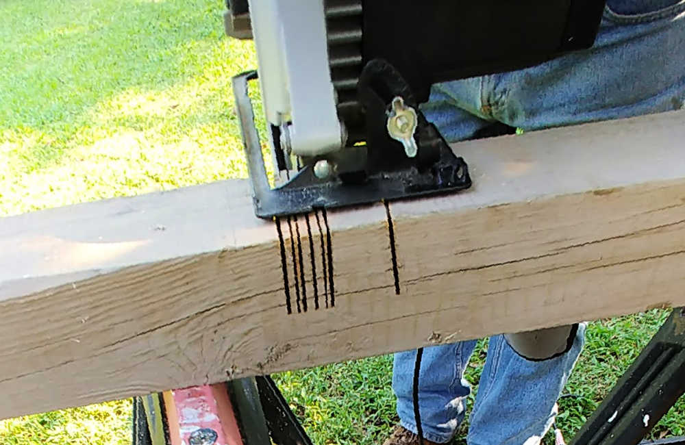 Man with saw making small cuts in a piece of 4 x 4 timber.