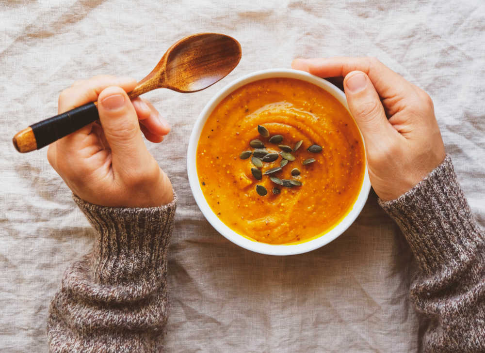 Hands with a spoon and bowl of pumpkin puree and pumpkin seeds.