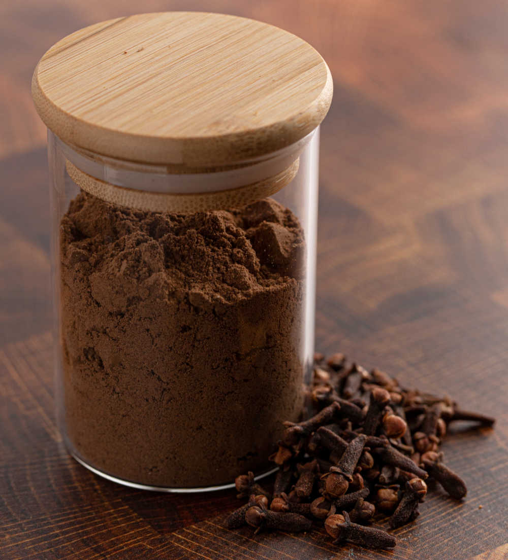 Ground cloves in a jar sitting next to whole cloves.