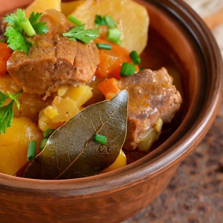Meat and vegetables in a bowl with a bay leaf.