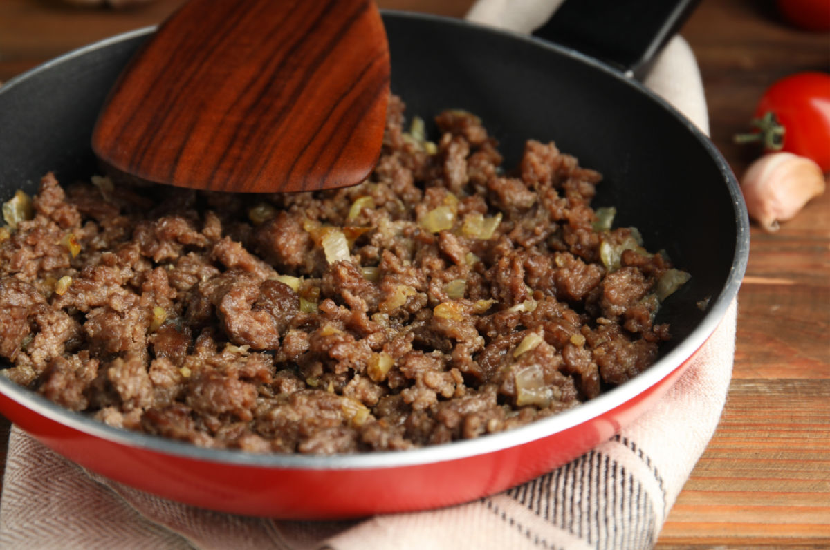 Cooking ground beef and onions with garlic in a frying pan.