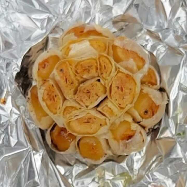 A head of roasted garlic with the tops of the cloves trimmed off sitting in aluminum foil, which has just been cooked following a roasted garlic recipe.