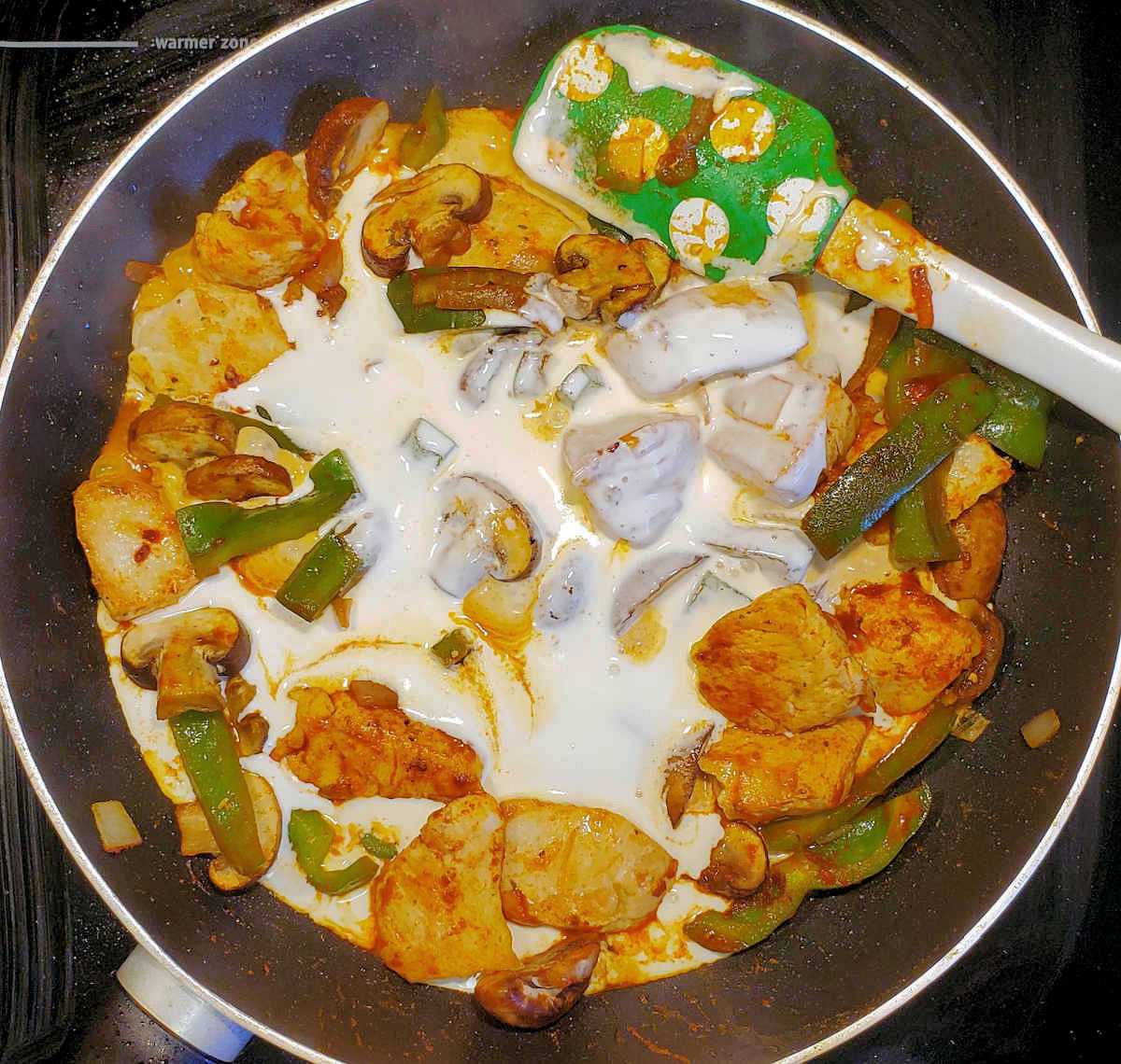 A non stick pan and green spatula stirring pollo en crema.