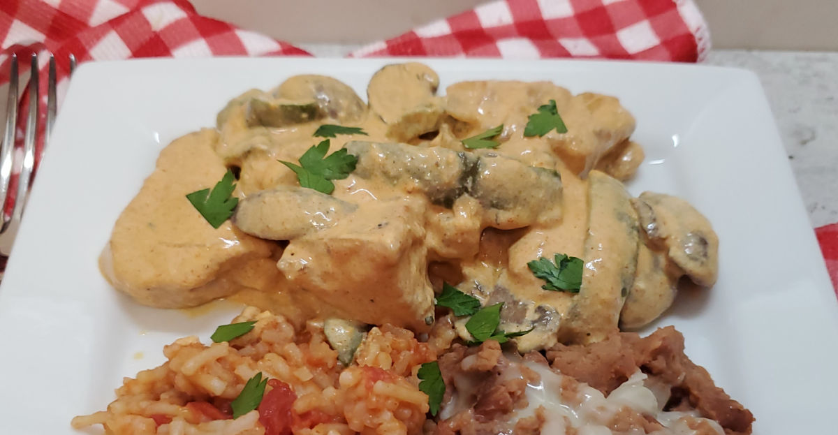 A white plate on a red and white checked napkin showing a closeup of pollo con crema.