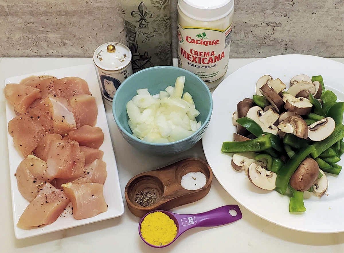 Chicken pieces, onions, mushrooms, peppers, salt and pepper, chicken granules, paprika, olive oil and Mexican crema on a countertop - ingredients for pollo con crema.
