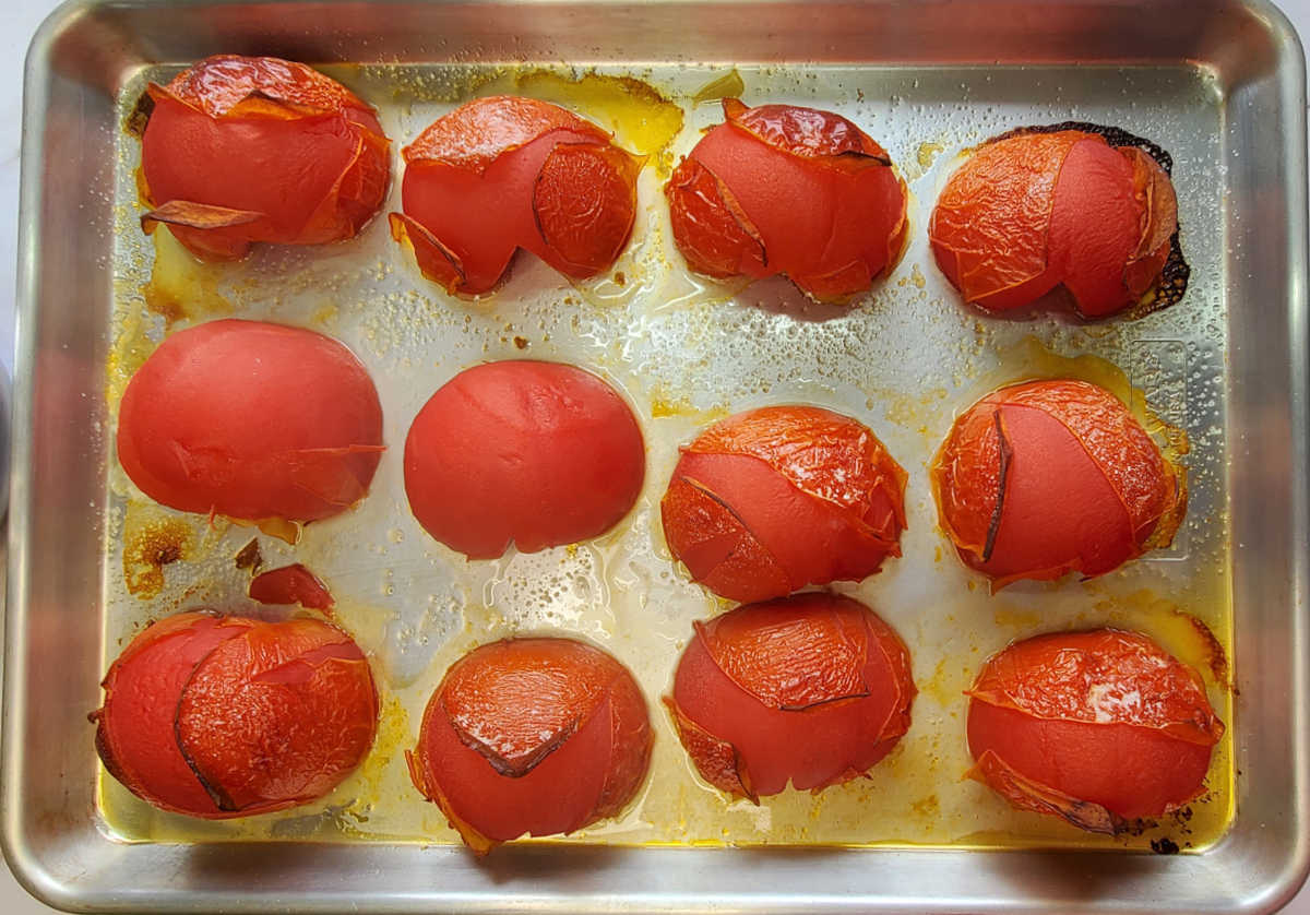 Roasted beefsteak tomatoes on a baking pan with skins that have torn and wrinkled.