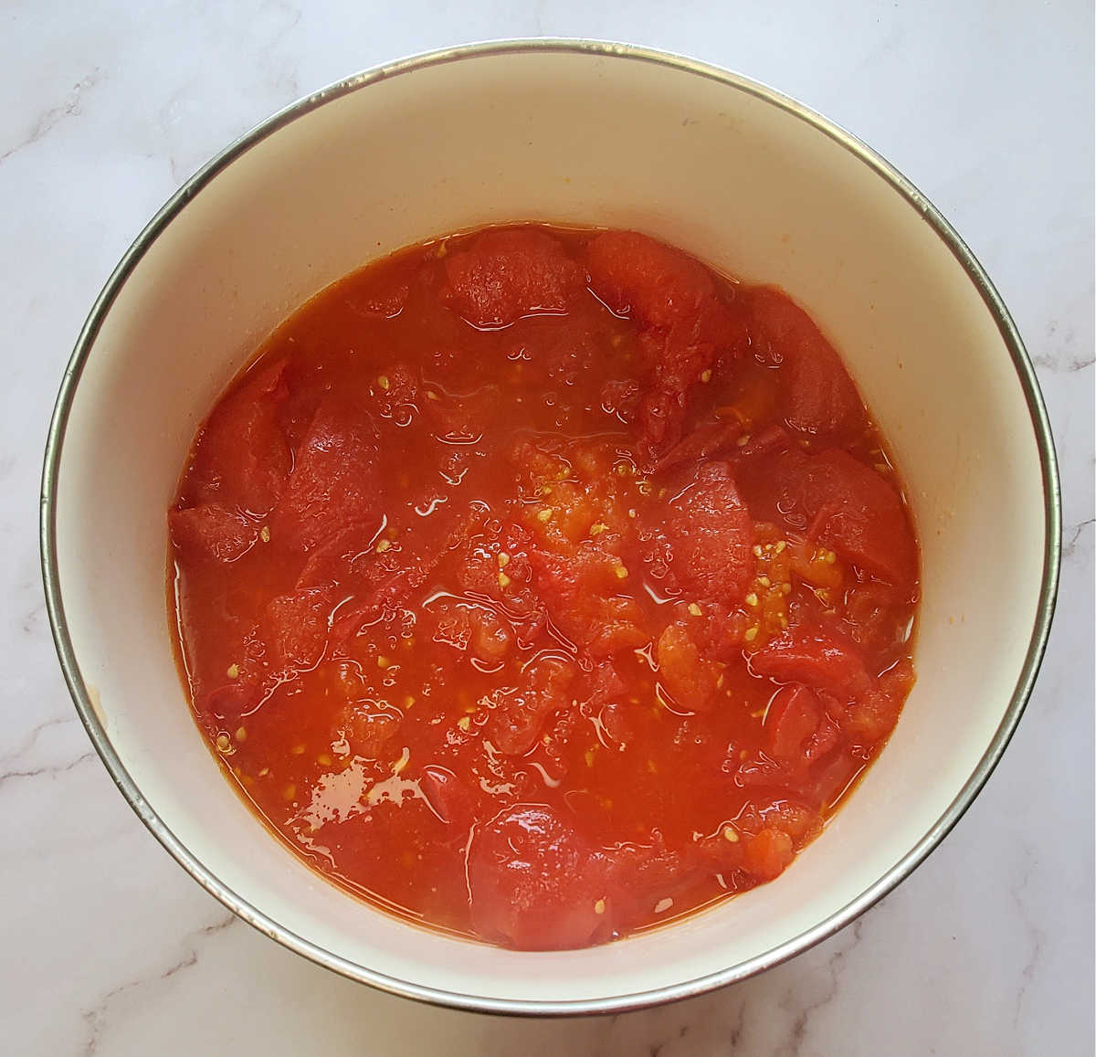 Crushed roasted tomatoes for sauce in a white bowl on a marble countertop.