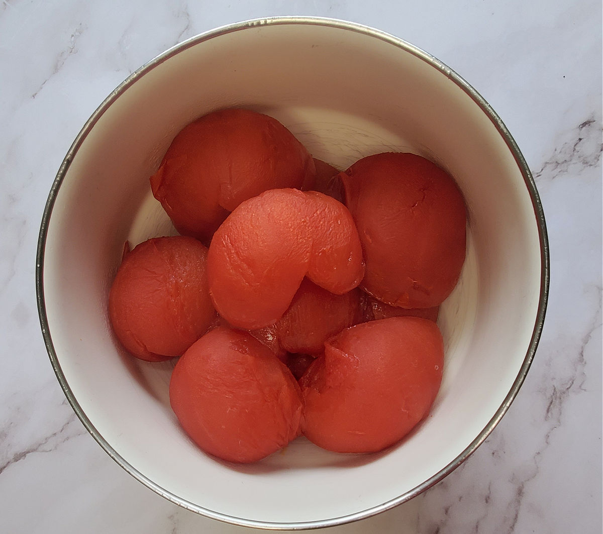 Roasted beefsteak tomato halves in a white ceramic bowl on a marble countertop.
