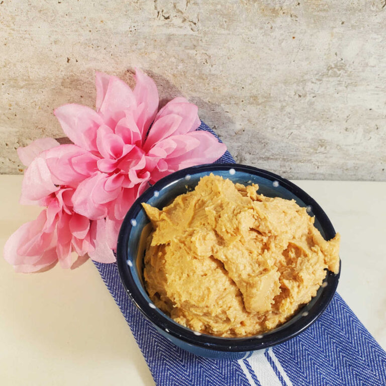 Peanut butter and cream cheese frosting in a blue bowl with a blue striped towel and pink flower.