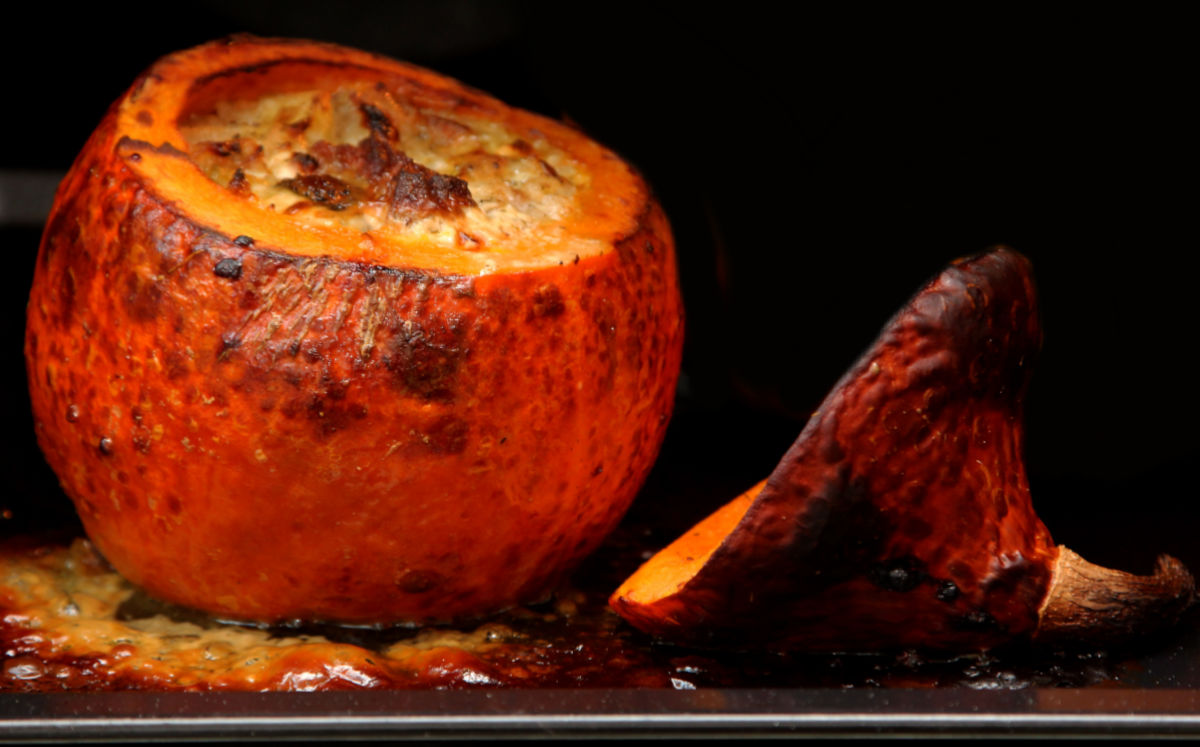 Pumpkin dip in a pumpkin bowl baking in the oven with the lid of the pumpkin.