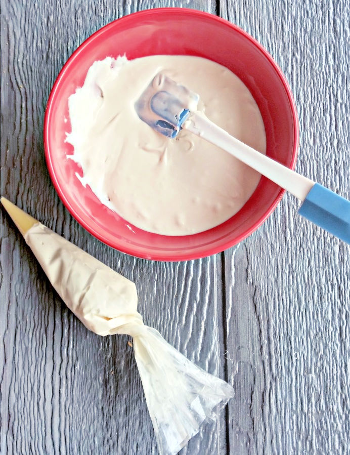 Royal icing for Gingerbread Houses Royal icing in a red bowl with a blue spatula next to an icing bag filled with the icing and ready to decorate a gingerbread house.