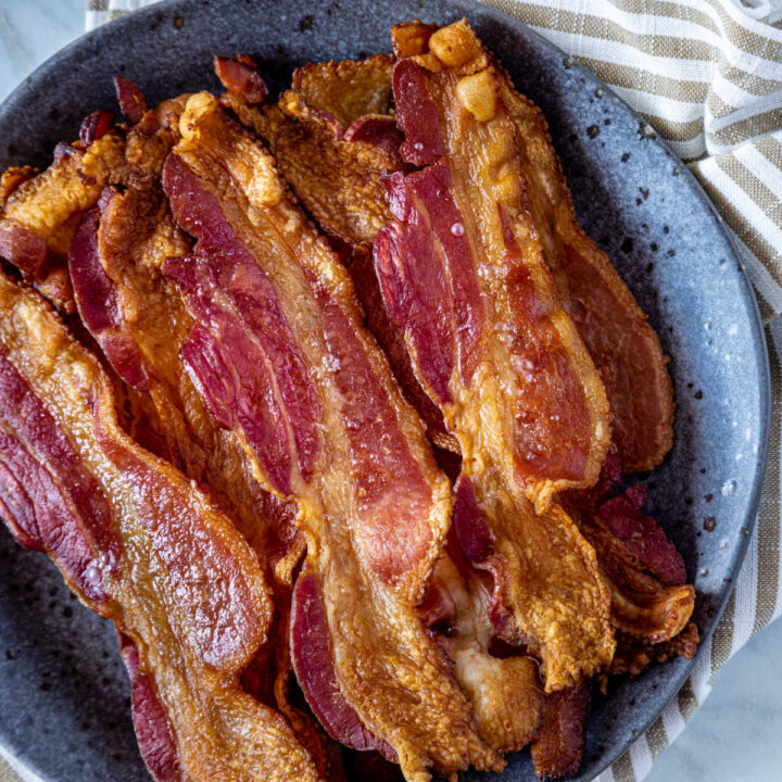 Crispy oven-baked bacon in a blue bowl next to a striped towel.