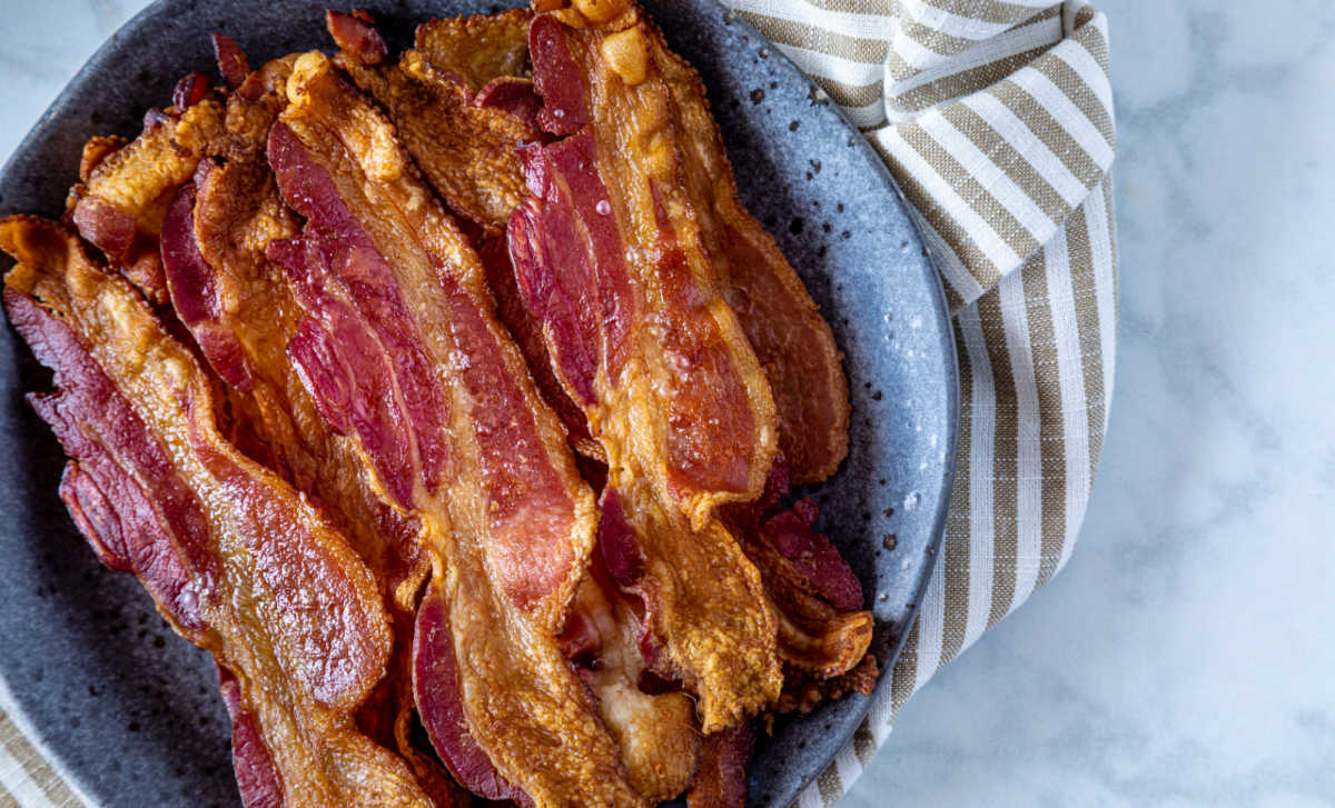 No mess oven bacon in a blue bowl next to a striped towel.