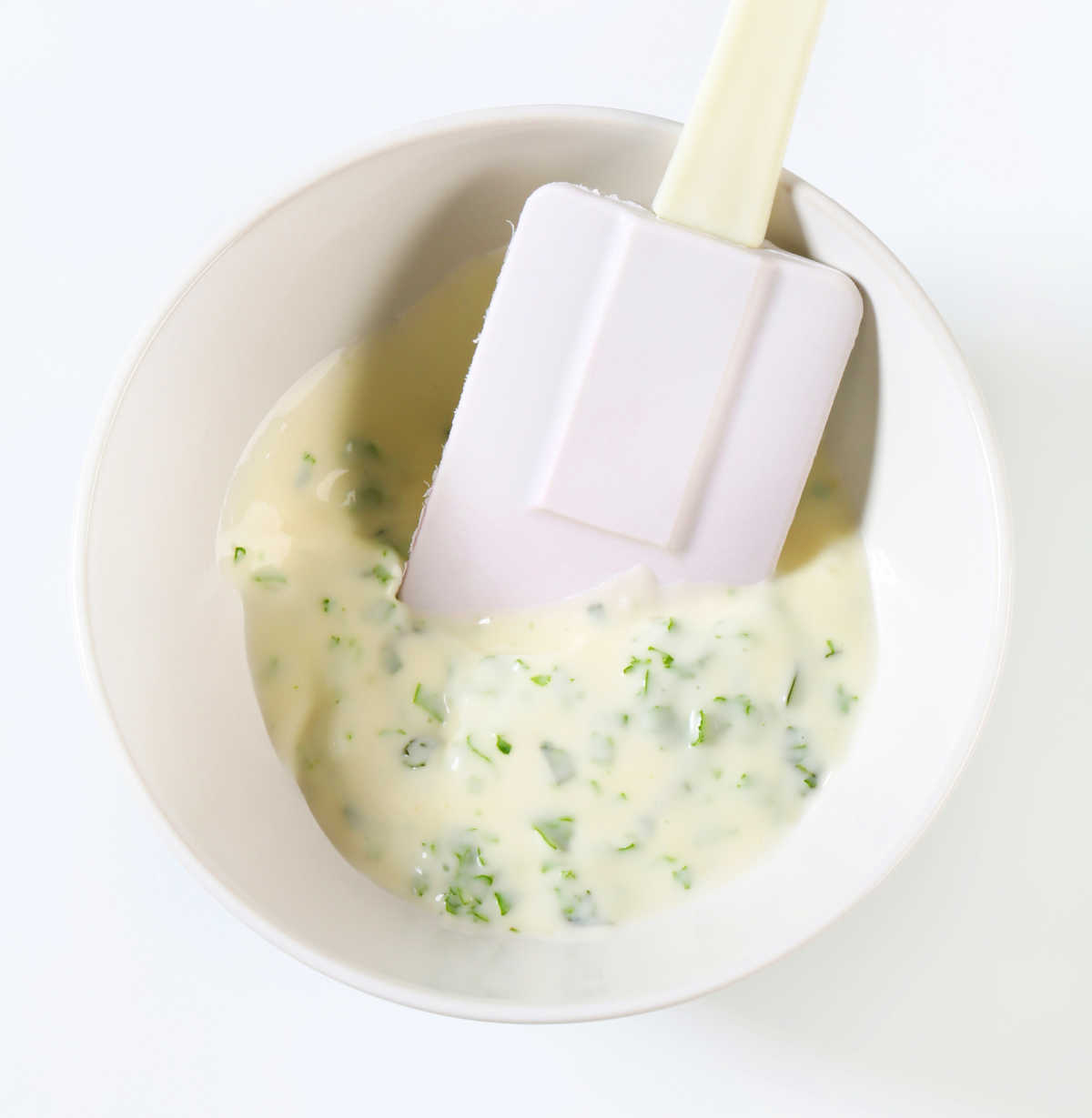 Thickened sauce with herbs in a white bowl with spatula.