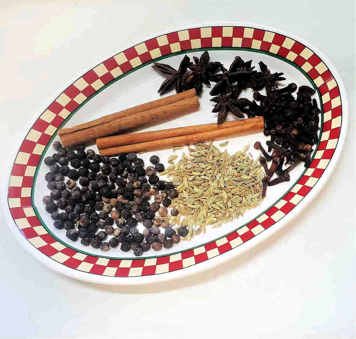 A red checked dish holding ingredients for Chinrest 5 spice powder: cinnamon, star anise, peppercorns, fennel seeds ,and cloves.