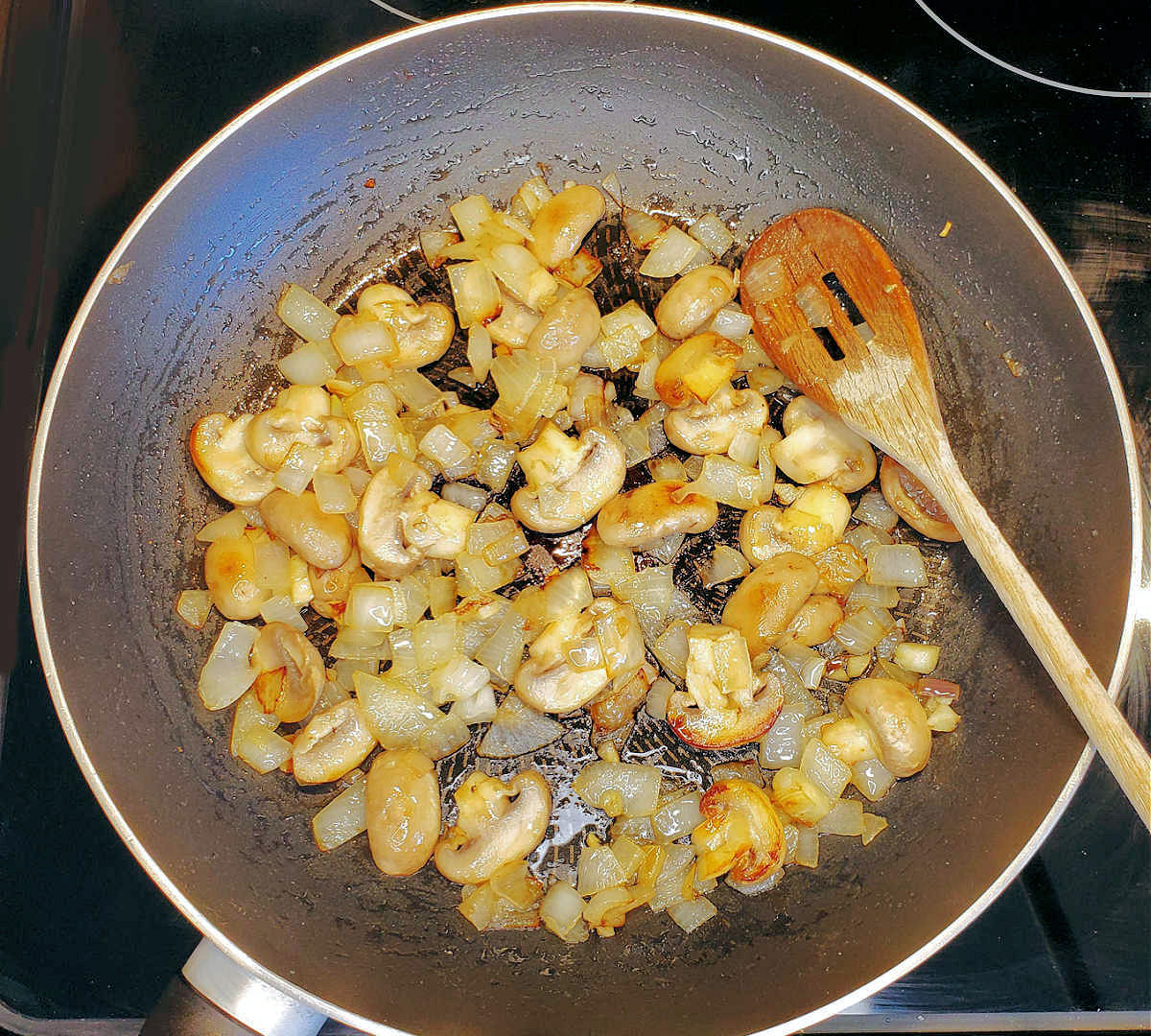 Mushrooms and onions in a skillet with a wooden spoon, cooking to make an Irish steak sauce.