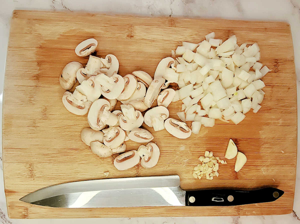 Mushrooms, onions and garlic on a cutting board with a knife, ready to make a whiskey steak sauce.