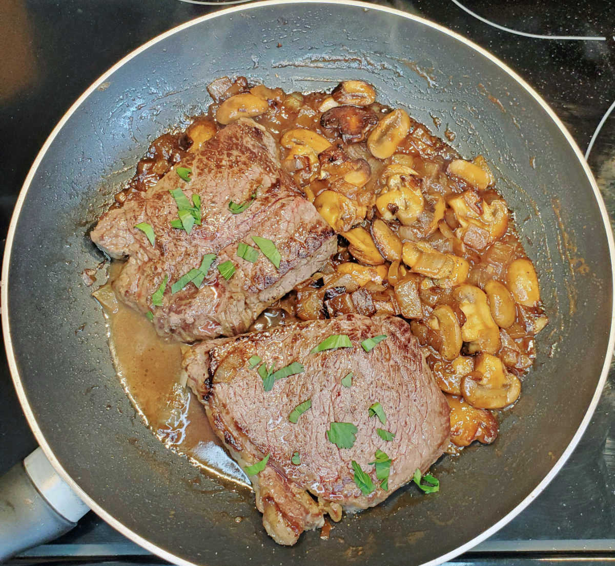 Sirloin steak with whiskey sauce in a large skillet with onions, garlic and mushrooms.