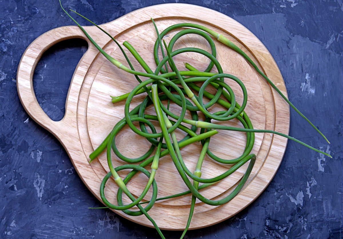 Curled green garlic scapes on a wooden cutting board.