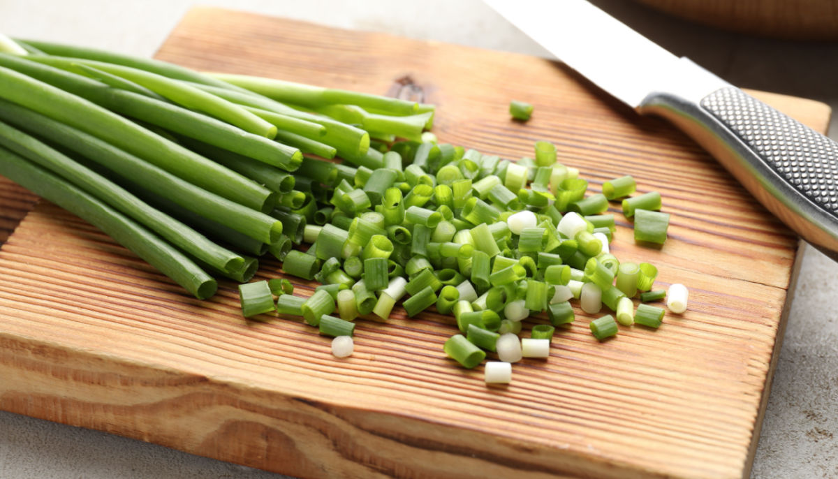 The light green and white slices of scallions on a cutting board with a knife.