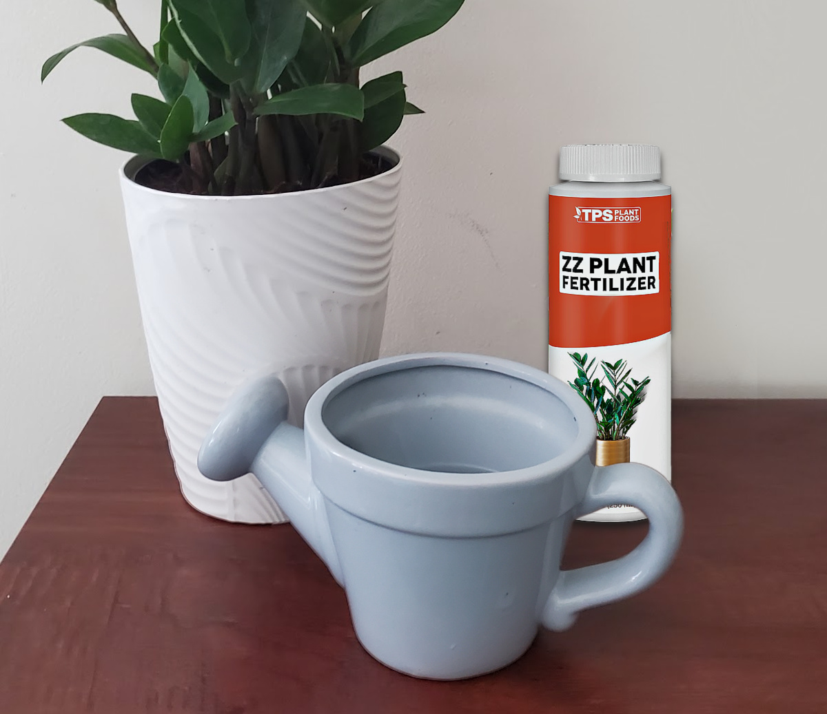 ZZ plant, watering can and bottle of plant fertilizer on a wooden table.