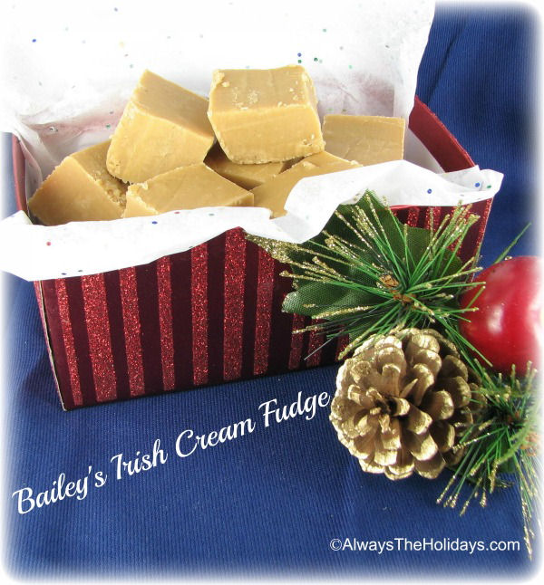 A red striped box filled with Bailey's Irish cream fudge for Christmas next to a spray painted gold pine cone and faux pine boughs.