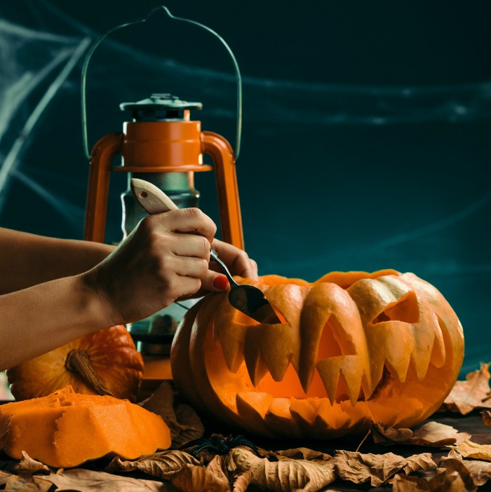 Woman carving a pumpkin next to fall leaves and a lantern.